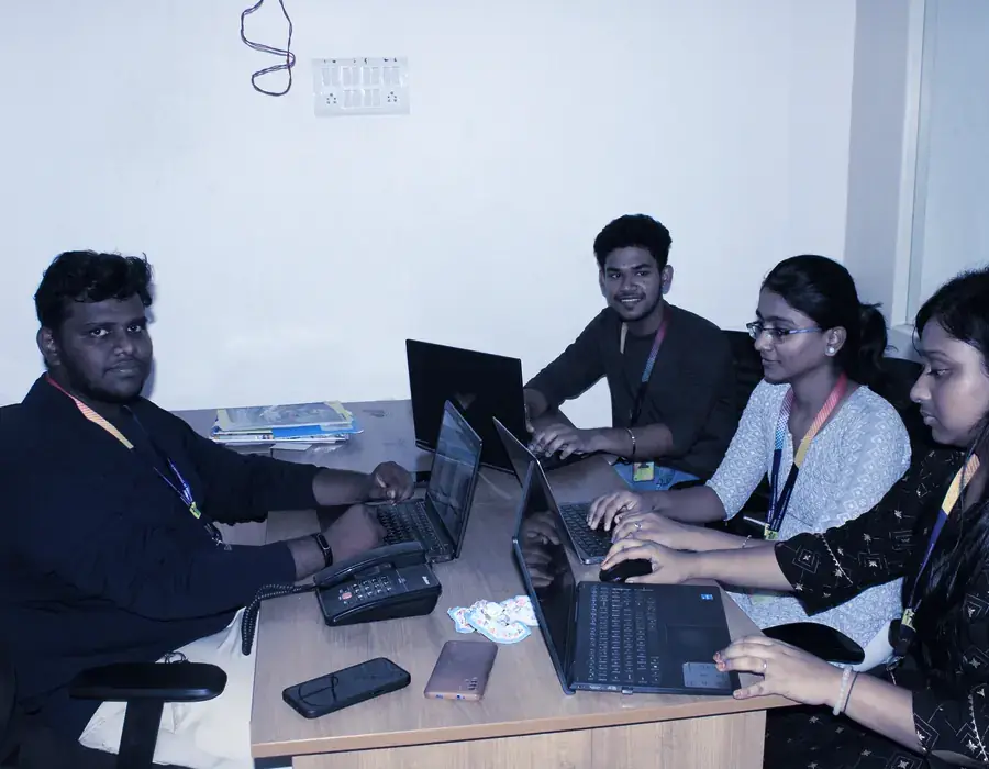 Four interns working at a desk with laptops